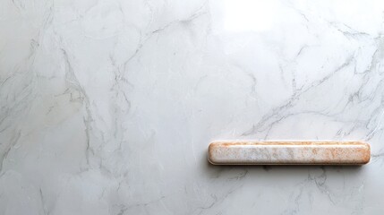 A smooth marble surface with subtle veining, featuring a wooden rolling pin positioned horizontally across the scene.