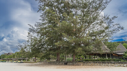 The beach of the resort hotel. A row of sun loungers under umbrellas in the distance. Roofs of...