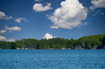 Lake Joseph in Muskoka, Ontario, Canada. A clear summer day with blue water stretching to a tree-lined shore dotted with cottages, creating a serene and picturesque setting.