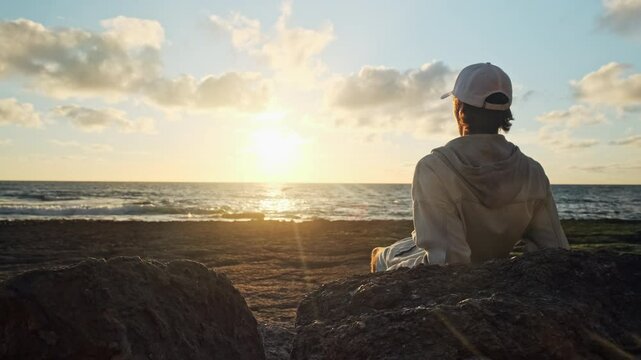 Man on a beach is looking distance during beautiful summer sunset. Human looks to the sun over horizon in  morning while sunrise. Happy person contemplates the beauty of nature. Freedom. Slow motion