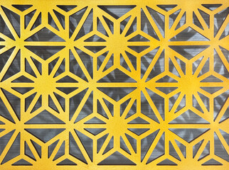 Close up of geometrical hexagon and flower shape pattern. 3D cutout laser cut star and geometric flower shapes carved from wood finished in metallic gold paint. Seamless background texture.