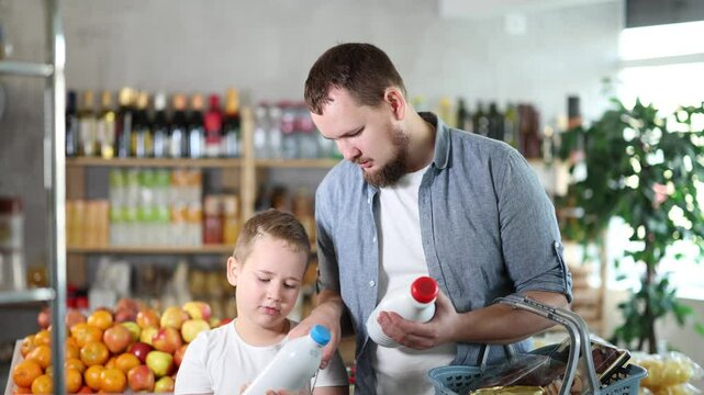Man with son hold packages bottles and choose consider milk in store. Market visitor choose consider make choice bottle milk. Client hesitates before buying, chooses drink, reads labels on bottles