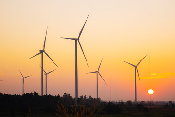 Wind turbines harnessing wind power during sunrise, set in an expansive agricultural landscape.