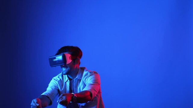 Smart gamer wearing VR goggles while holding sword and fencing in virtual world. Attractive male model playing action game while standing at blue background and accessing in metaverse. Apparatus.