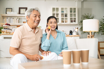 Asian senior couple playing toss ping pong ball to the cup in the living room at home on weekend...