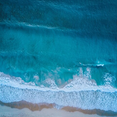 Aerial view of turquoise ocean waves breaking on a sandy beach