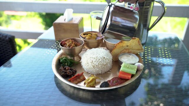  Nepali Thakali set on a thali: rice, black dal, chicken curry, greens, pickles, papad, yogurt, with ghee poured over rice, served outdoors.