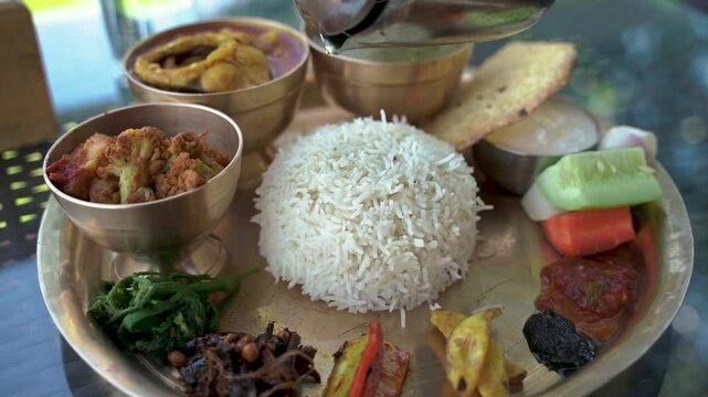 A closeup of traditional nepali thakali set, with steamed rice topped with ghee, surrounded by dal papad, meat, and tangy pickles.