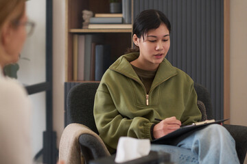 Portrait of teenage girl doing assessment tests during therapy session with female psychologist