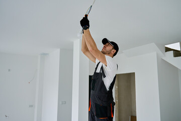 Professional electrician wearing gloves installing light bulb in ceiling socket. Home electrical...