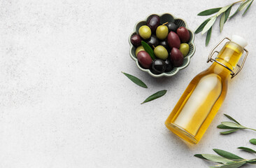 Olive oil bottle and bowl of green and black olives with olive branches on marble background