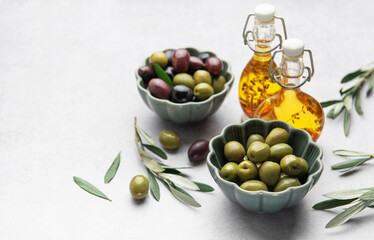 Bowls of green and black olives with olive oil bottles and olive branches on marble table