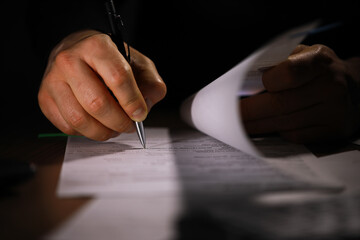 Close-Up of Hand Signing Documents with Pen in Dimly Lit Office Setting