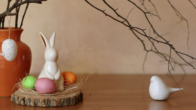 easter decor with bunny. hands hanging eggs on branches in a vase on the table
