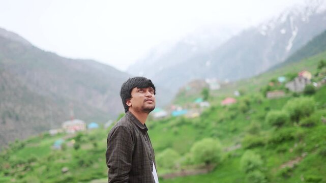 4K Portrait shot of an Indian man walk in front of Triloknath village with snowy Himalayas in background at Lahaul in Himachal Pradesh, India. Tourist walking in front of the snowy Himalayas.