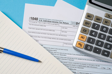 Top view of tax forms, calculator and pen on blue table