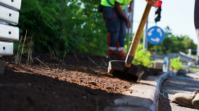 Low angle close-up of workers spreading soil at road curbs on highway ramp construction site