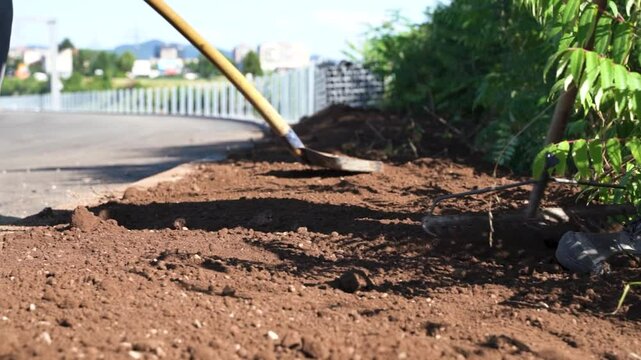 Low angle close-up of workers spreading soil with shovel and rake at road curbs on highway ramp construction site
