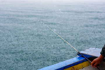Obraz premium Fishing rod in the boat under the rain. Fishing rod, sea, boat and rain.