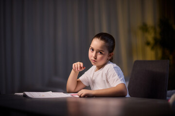A young child is deeply engaged in thought while completing their homework during a late night