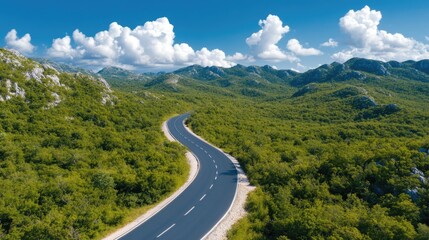 Obraz premium Serene mountain highway winding through lush green forest under blue sky with fluffy clouds