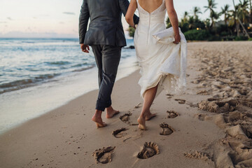 Couple walking on a beach at sunset, leaving footprints in the sand after a wedding ceremony