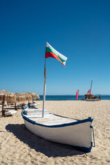 Sunny day at the beach where the Bulgaria flag flies beside colorful umbrellas and water sports activities. vertical