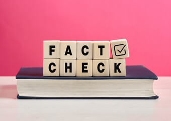 Wooden cubes showing fact check on a book with pink background