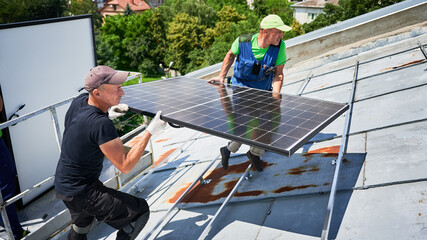 Workers building solar panel system on metal rooftop of house with assistance of crane lift. Two...