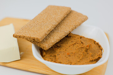 In close-up on a wooden board there is a white plate with liver pate, slices of bread lie on top and a piece of butter on a white background next to it. The concept of healthy food, a healthy snack