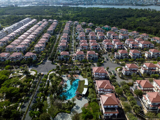 Modern, luxury Housing estate with swimming pool, houses, and villas in rows, beautiful landscaping on sunny, clear morning from aerial view. Wide view with river as background.
