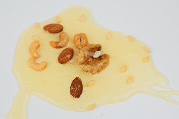 In a yellow puddle of liquid honey lie a mix of nuts on a white background in close-up. The concept of a healthy snack, a natural dessert, sweet. High quality photo