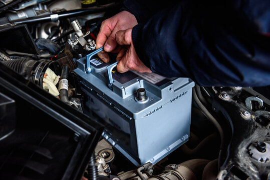 A man installing a new car battery under the hood of a car. Vehicle maintenance and repair.