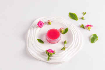 Cosmetic jar with pink lip balm on a white embossed tray with small Kalanchoe flowers. Natural lip skin care. top view. Daily lip care