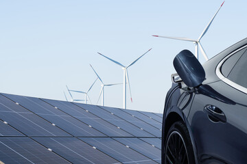 Close up of electric car with a connected charging cable on the background of solar panels and wind...