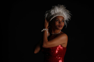 Low key portrait of young curly woman in red dress with headdress made of bird feathers
