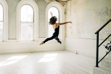 Ballet dancer in black leaps gracefully in a bright vintage studio