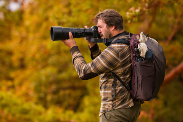Nature photographer. Young male photographer autumn season outdoors portrait. Side view. Landscape photographer taking photos.
