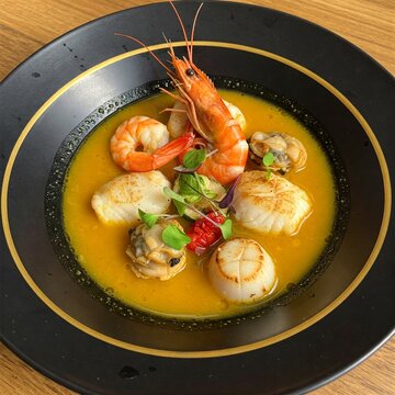 creative fusion version of Parihuela, served in a minimalist modern black bowl with gold-rimmed plating.