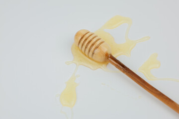 A wooden spoon lies in a puddle of liquid yellow honey on a white background. The concept of wholesome and healthy food, sweets, natural products. High quality photo