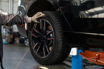 Serviceman checks car suspension on a column lift in car service.