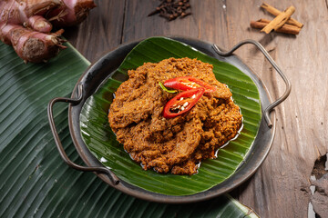A plate of beef rendang, a rich Indonesian dish cooked in coconut milk and spices, served on a banana leaf. Garnished with red chili slices, this festive meal is popular during Eid celebrations