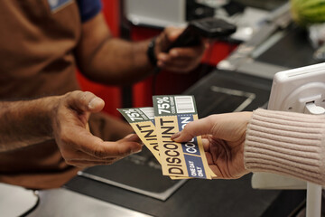 Closeup of female hand holding discount coupons for best deals and giving to cashier at supermarket...