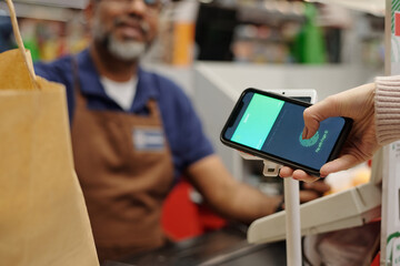 Closeup of unrecognizable female customer paying vis smartphone at supermarket checkout and scanning fingerprint for data and finance security, copy space