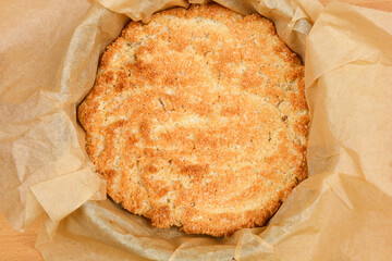 A top-down view of a baking mold lined with parchment paper containing a baked batter made from beaten egg whites and coconut, showing a golden brown surface