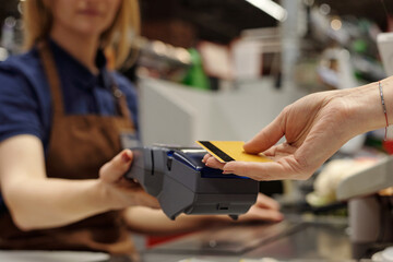 Closeup of unrecognizable female cashier handing banking terminal to customer paying via credit card at supermarket checkout, copy space