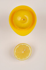 A top-down shot of a halved lemon on a yellow citrus juicer and a halved lemon beside it, both...