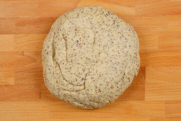 A top-down shot of unbaked sweet bread dough with poppy seeds, resting on a wooden surface, ready...