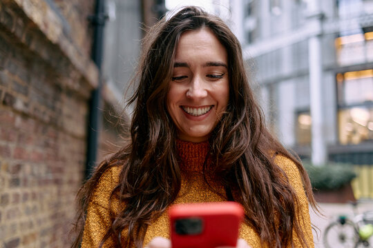 Woman smiling while using smartphone in urban setting - Powered by Adobe