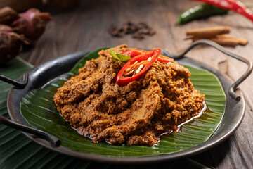 A plate of beef rendang, a rich Indonesian dish cooked in coconut milk and spices, served on a banana leaf. Garnished with red chili slices, this festive meal is popular during Eid celebrations